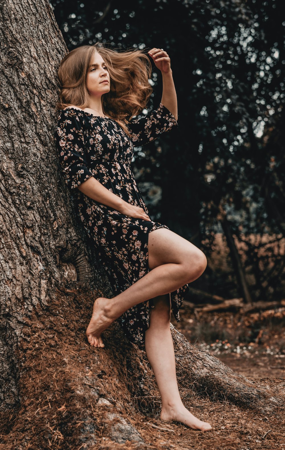 woman in black and white floral dress sitting on tree trunk