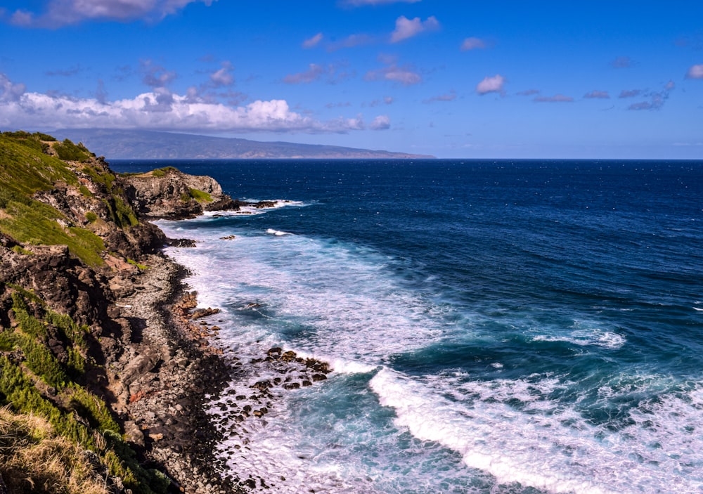 green grass covered mountain beside sea under blue sky during daytime