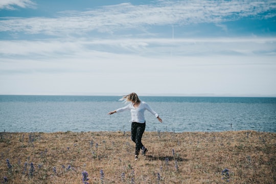 girl in white shirt and black pants walking on green grass field near body of water in Saaremaa Estonia