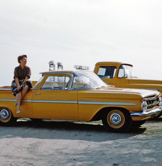 man in black jacket standing beside yellow vintage car