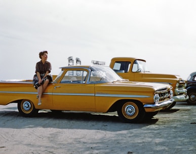 man in black jacket standing beside yellow vintage car