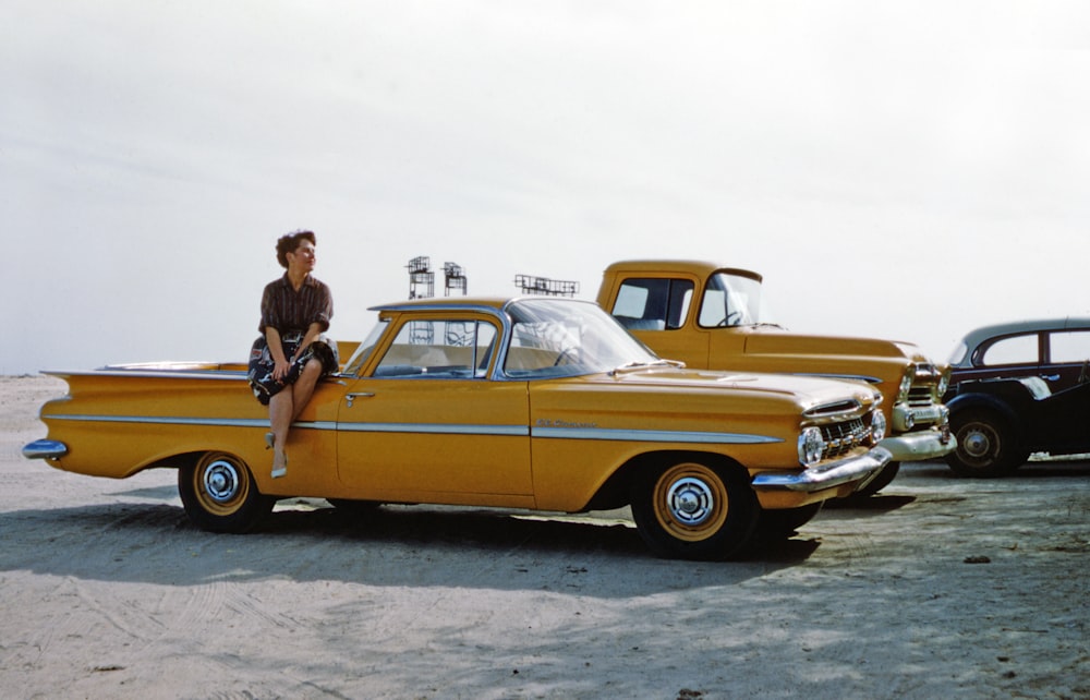 hombre con chaqueta negra de pie junto a un coche vintage amarillo