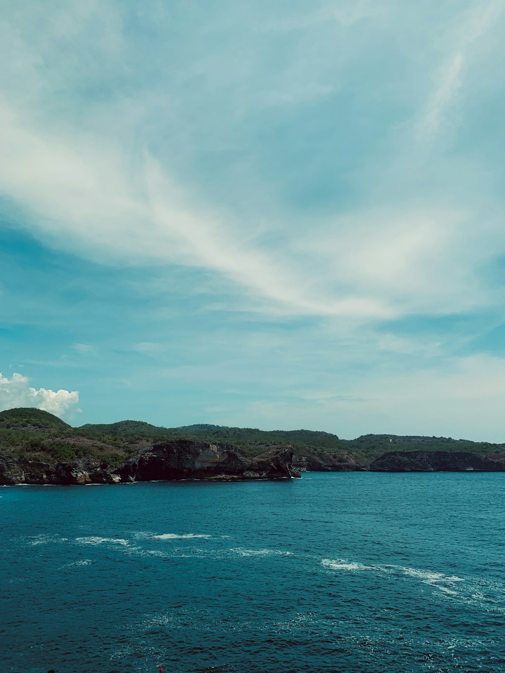 green and brown mountain beside blue sea under blue and white cloudy sky during daytime