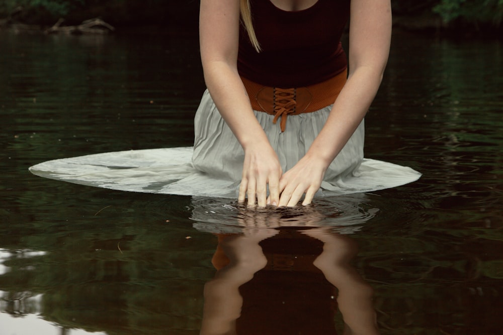 donna in canotta nera e pantaloni bianchi seduta sull'acqua durante il giorno