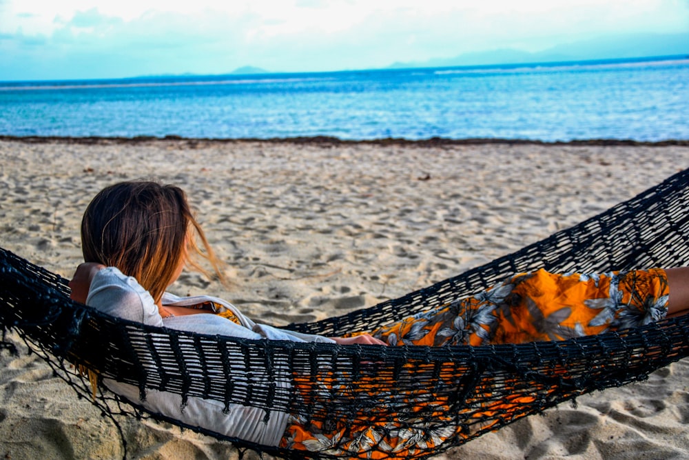mulher na camisa branca deitada na rede na praia durante o dia