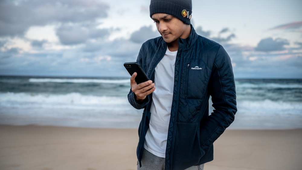 man in black leather jacket and gray denim jeans holding black smartphone