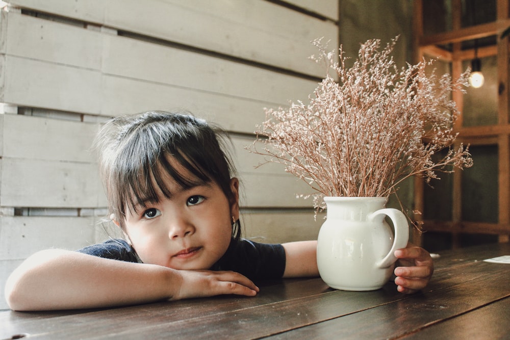 girl in black sleeveless shirt sitting beside white ceramic mug