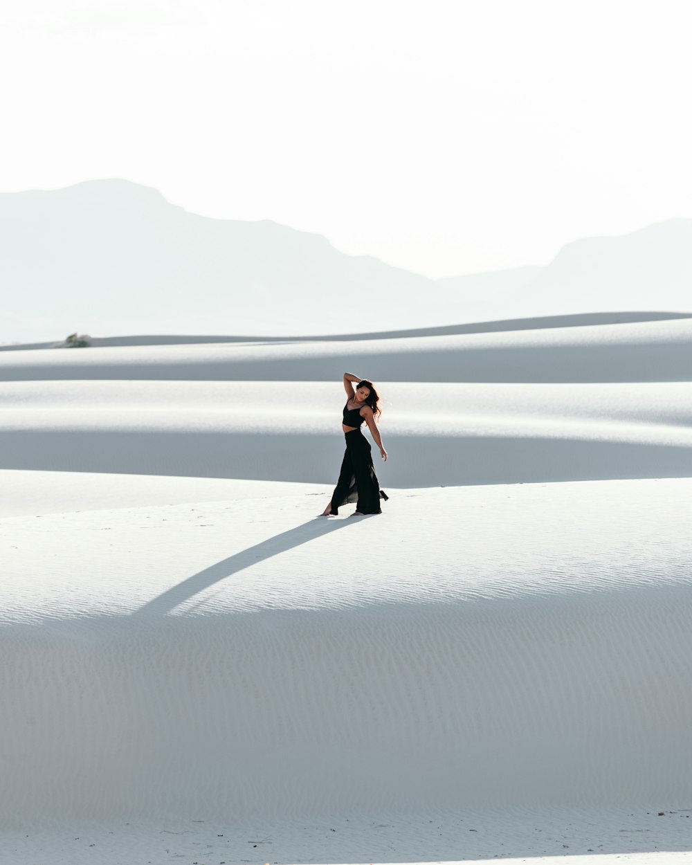 woman in black dress walking on white sand during daytime