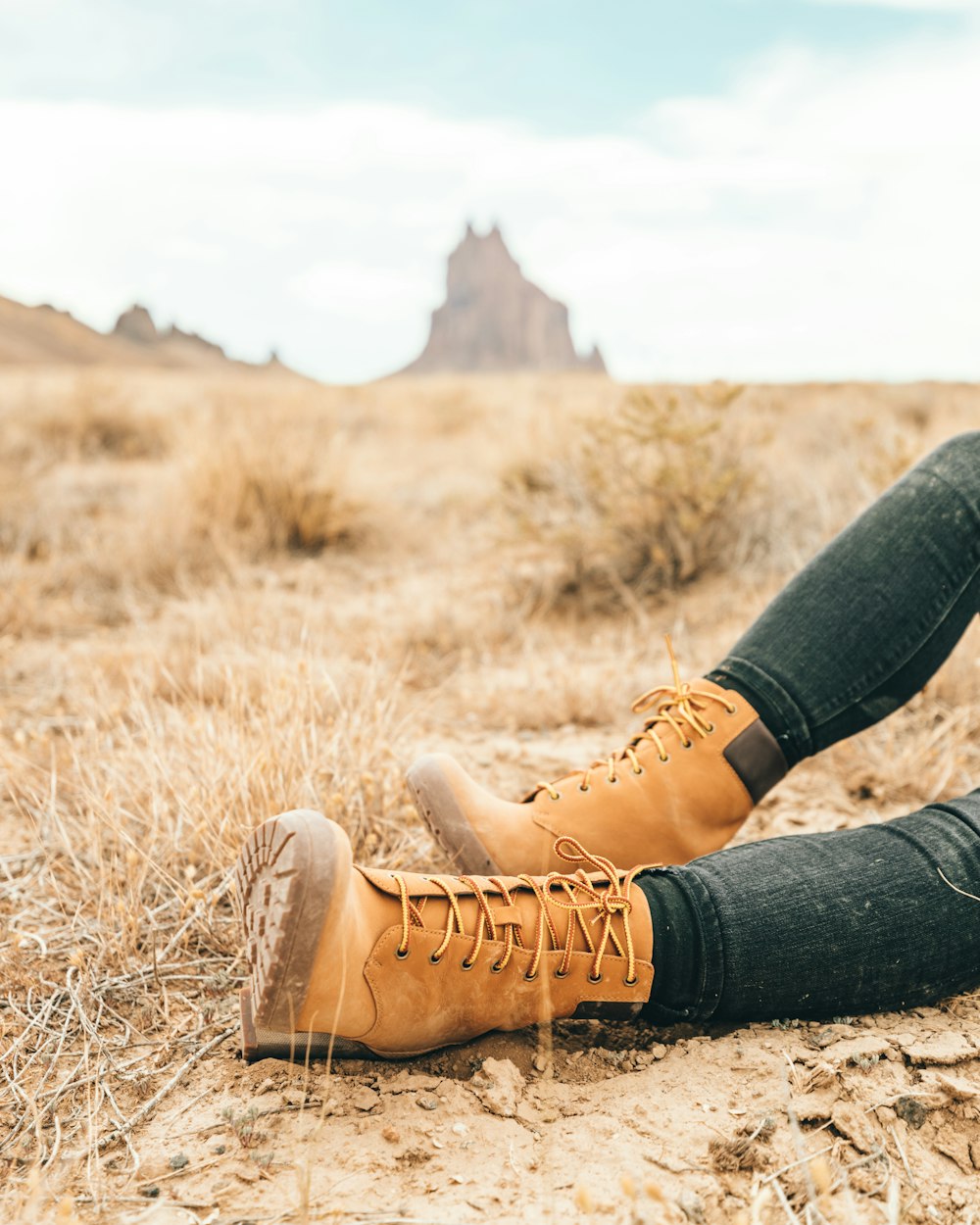 personne portant des bottes en cuir marron assise sur un champ d’herbe brune pendant la journée