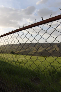 grey metal fence near green grass field during daytime
