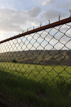 grey metal fence near green grass field during daytime