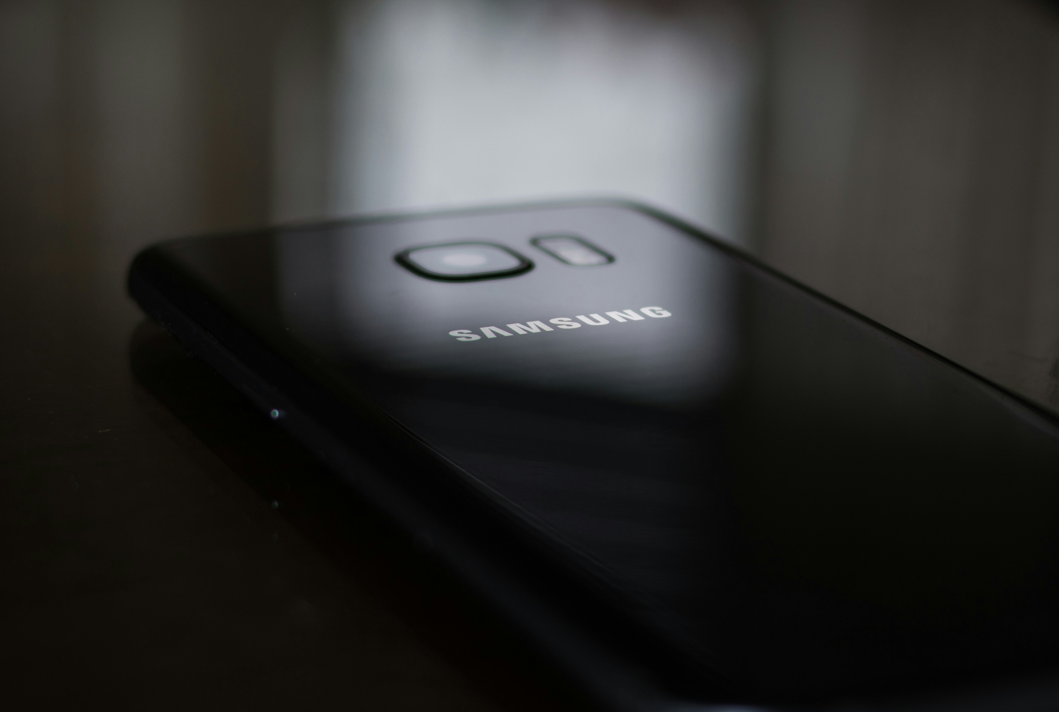 Sleek black smartphone with glowing screen on dark reflective surface, studio lighting