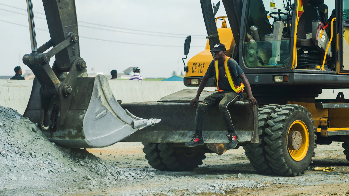 A construction worker in high-visibility clothing with heavy equipment on site