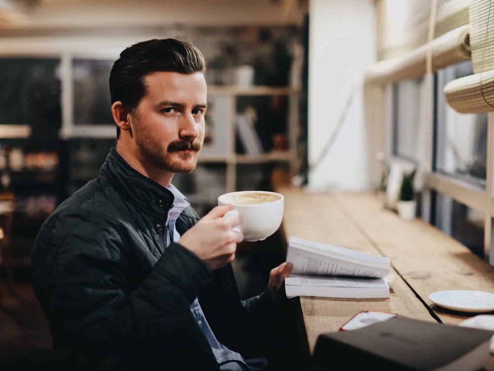 man in black leather jacket holding white ceramic mug