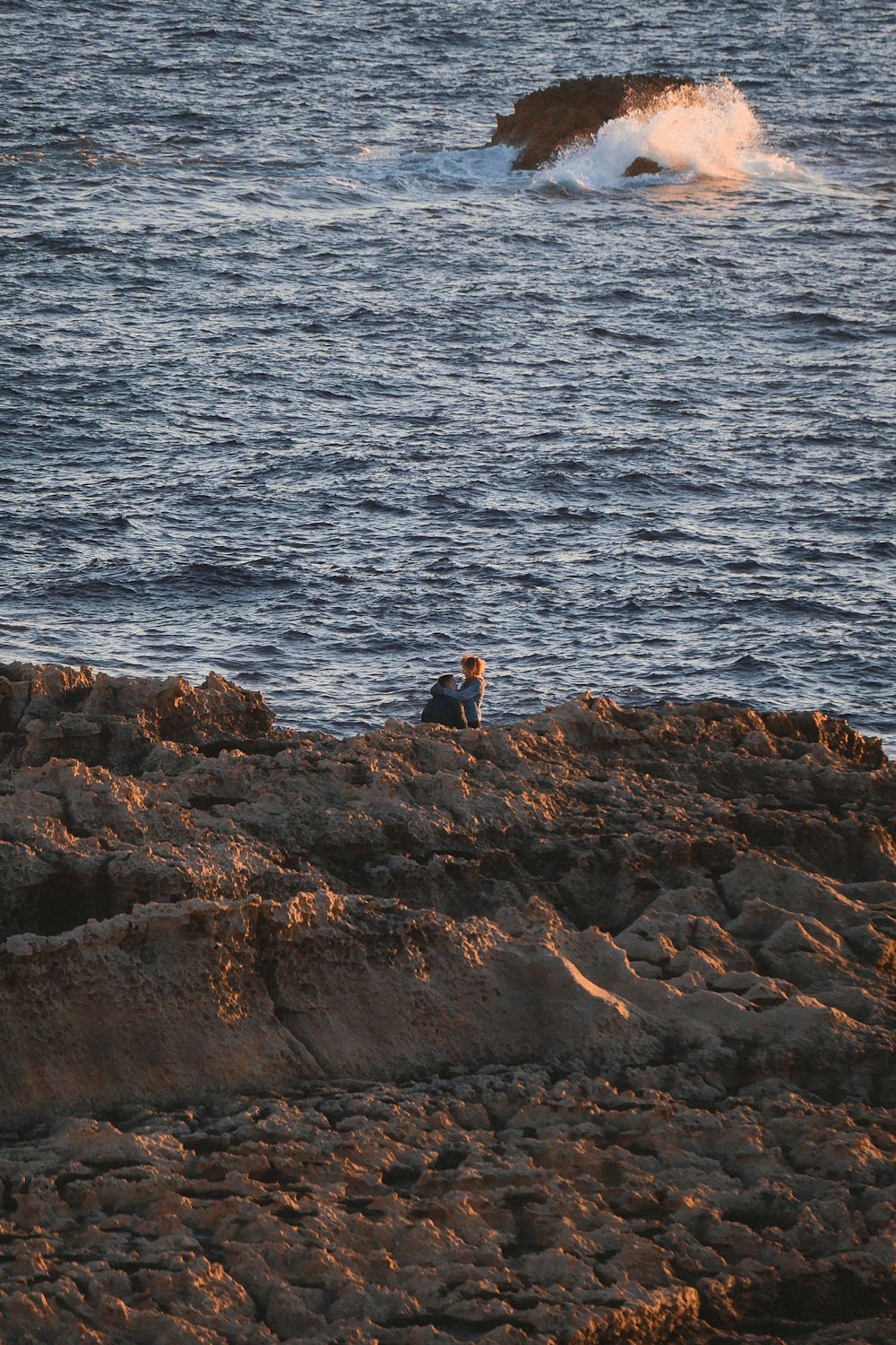 2 people standing on rocky shore during daytime