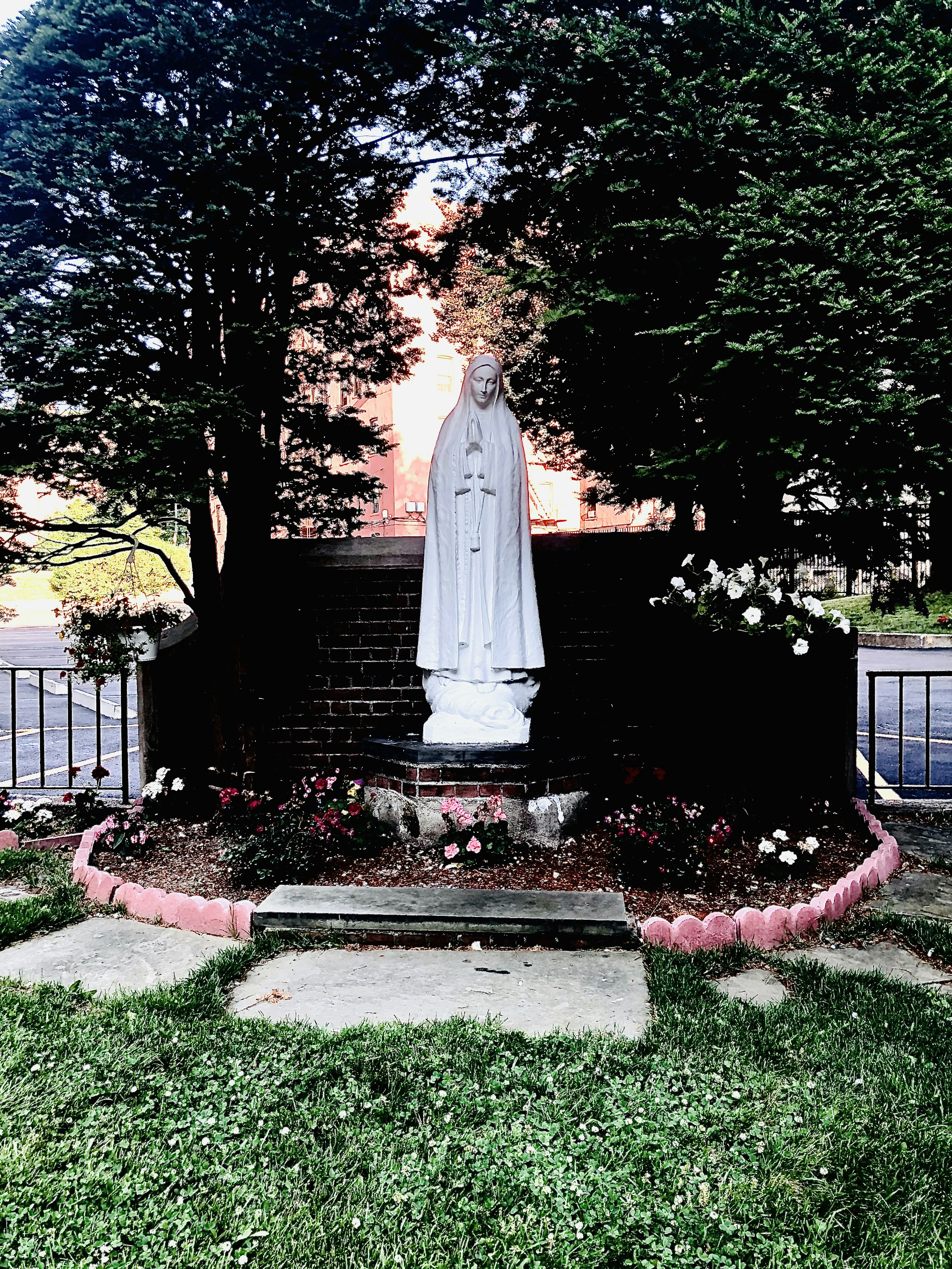 Peaceful Catholic garden with stone statue, lush greenery, soft sunlight, contemplative atmosphere
