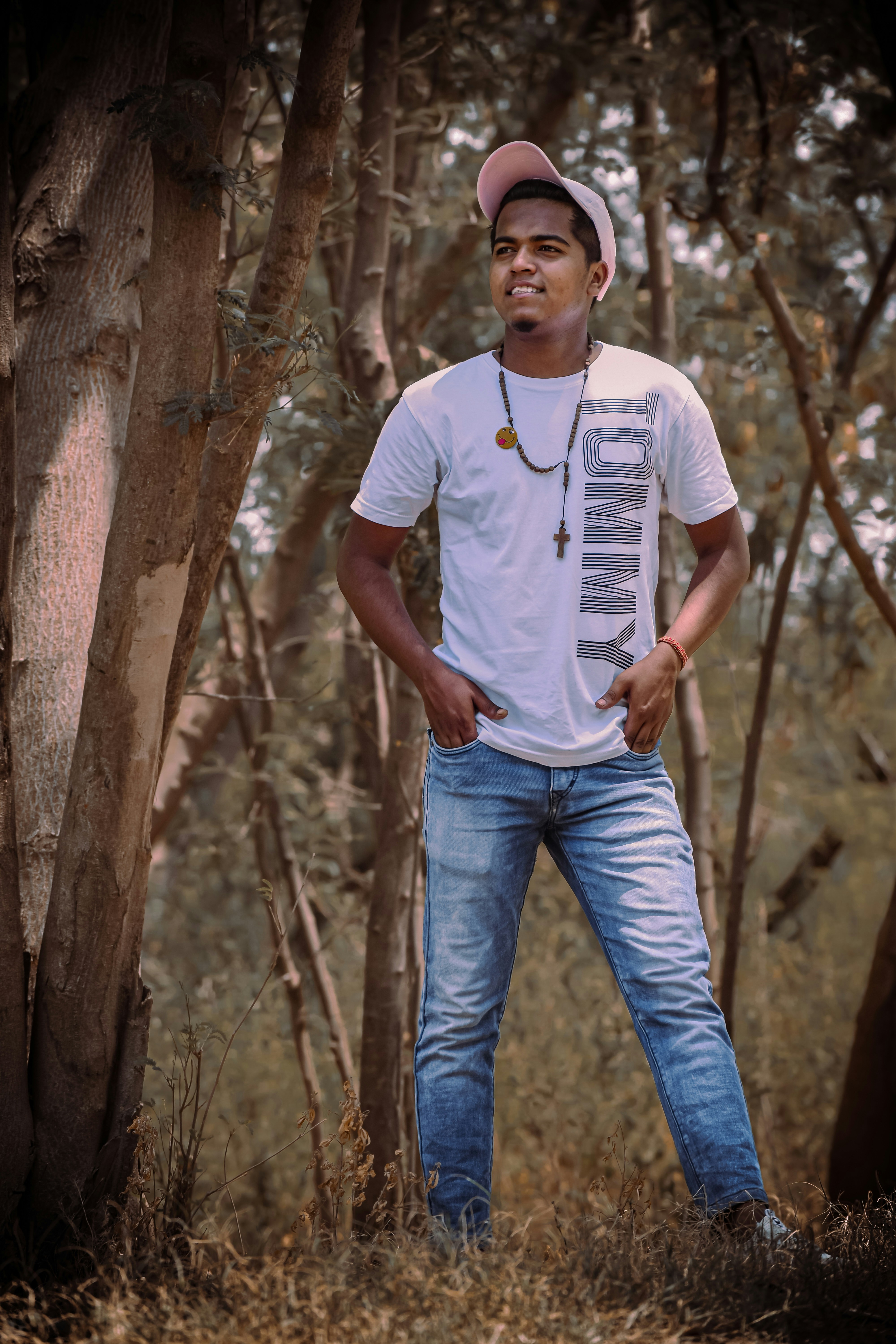 Pria dengan kaos leher kru putih dan jeans denim biru berdiri di samping pohon coklat selama
