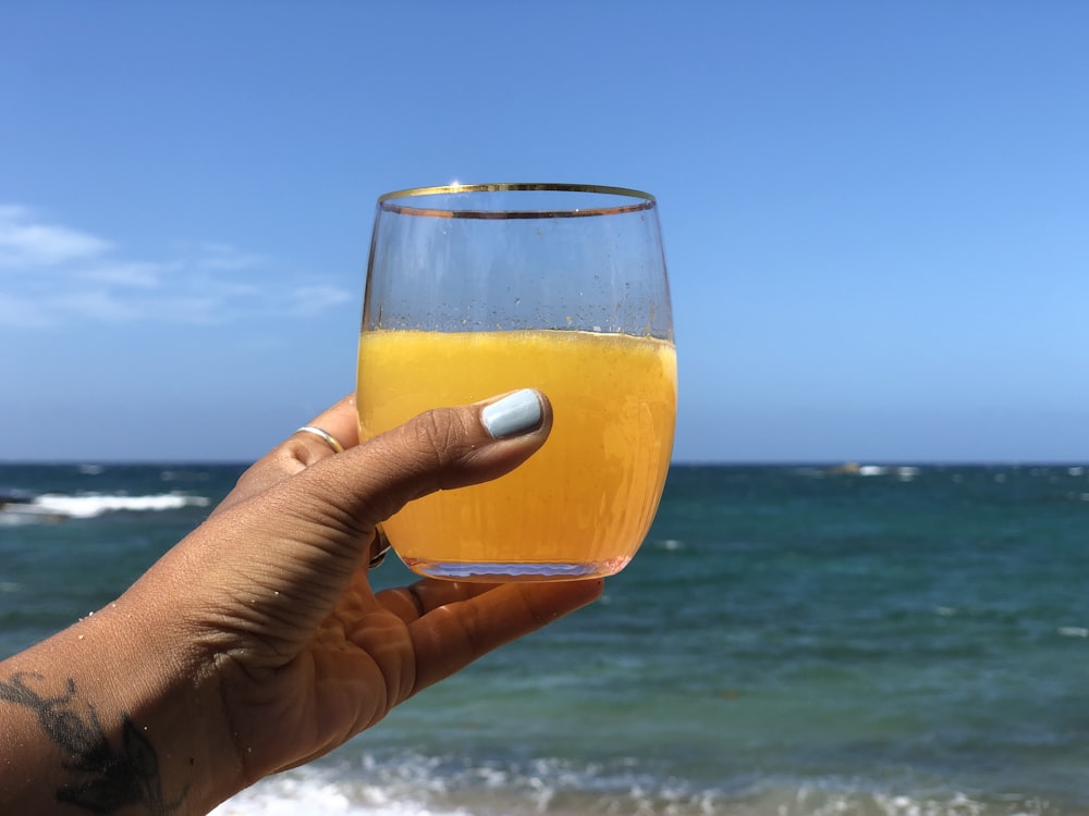 person holding clear drinking glass with brown liquid