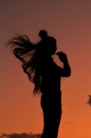 A silhouette of a woman with flowing hair standing under a stormy sky, illuminated by faint purple lightning.