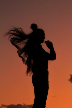 A silhouette of a woman with flowing hair standing under a stormy sky, illuminated by faint purple lightning.