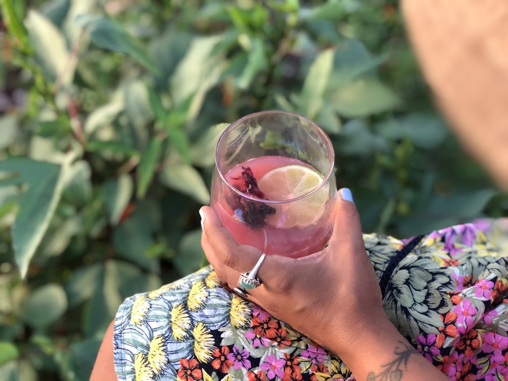 woman in blue white and black floral shirt holding clear drinking glass