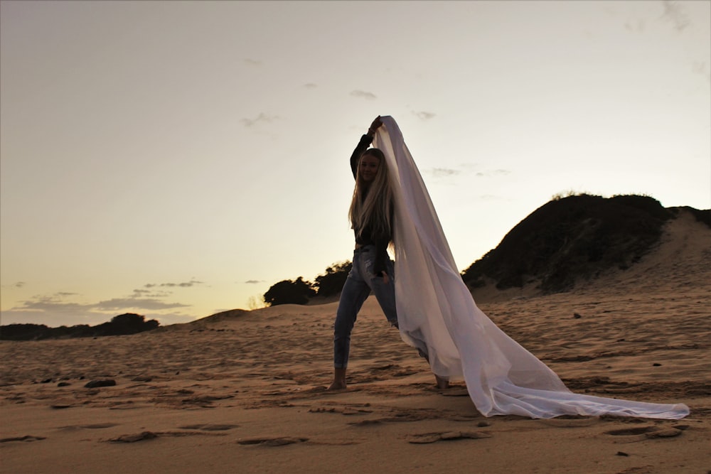 donna in vestito bianco che cammina sulla sabbia marrone durante il giorno