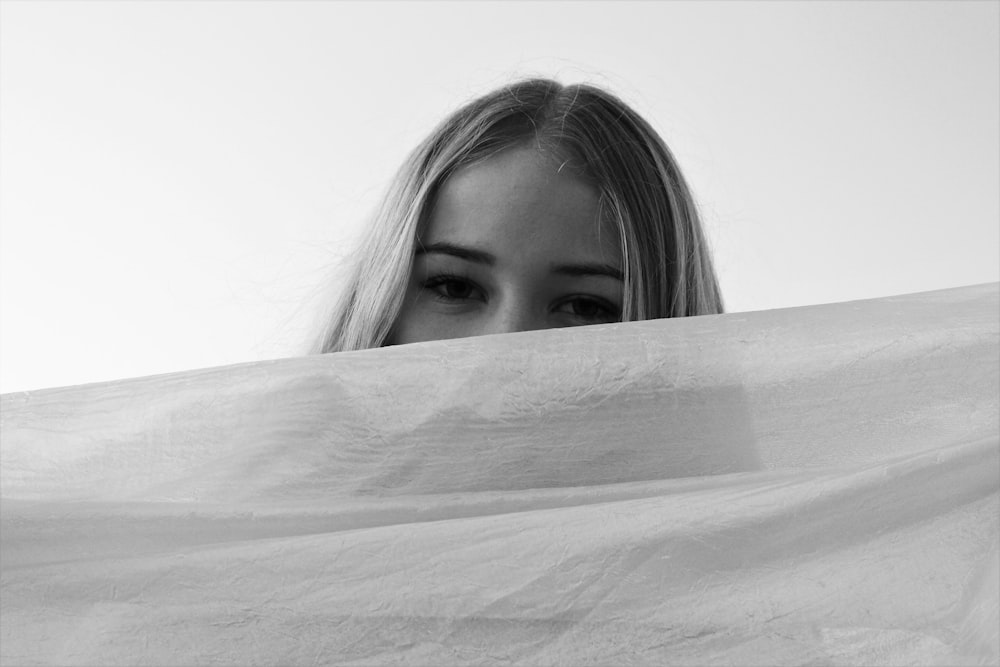 grayscale photo of woman covering her face with white textile