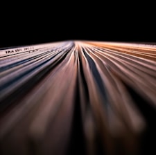 An extreme close-up of a book or stack of paper viewed from the side, showing the intricate pattern and texture of individual pages with shadows and highlights creating a sense of depth.