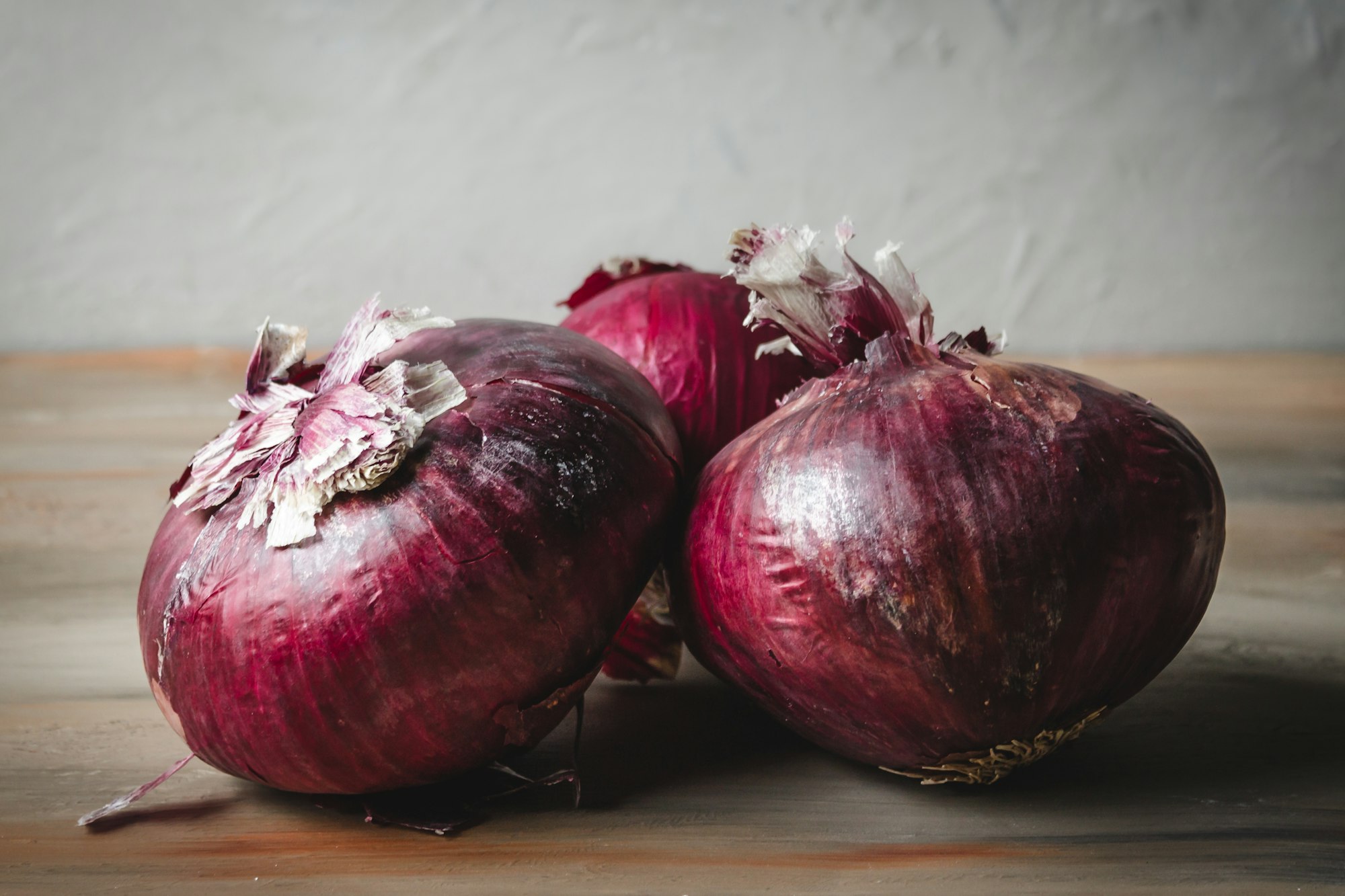Three red onions on a wood table
