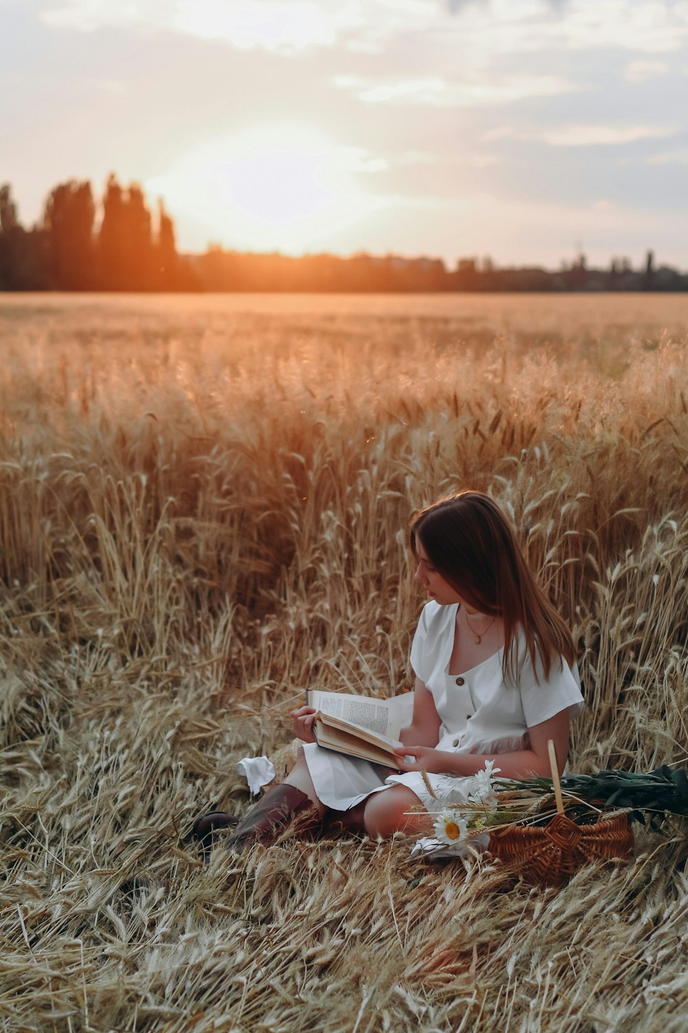 woman in white shirt reading book on brown grass during daytime