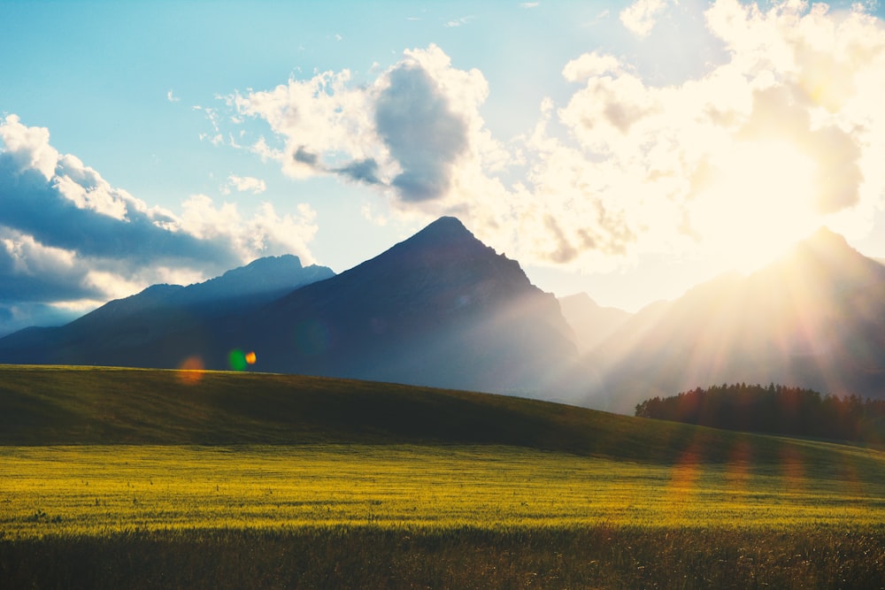 green grass field near mountain under white clouds during daytime