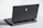 A sleek, dark laptop with a futuristic design, showcasing a blue alienware logo on its back cover. The laptop has a robust hinge, visible ventilation slots, and several ports at the back. It's placed on a light gray surface, with part of the slightly open keyboard in view.