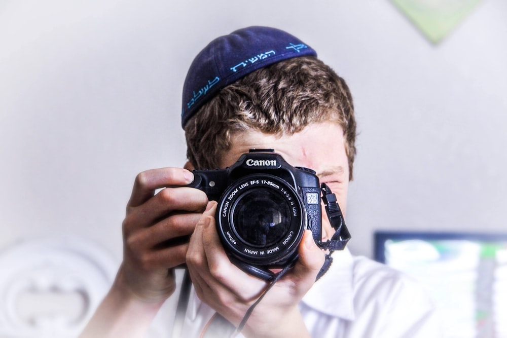 Homme en bonnet en tricot bleu tenant un appareil photo reflex numérique Nikon noir et argent