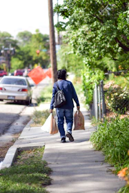 A friendly assistant carrying grocery bags with a smile in a neighborhood setting.