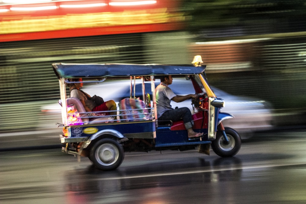2 men riding on red and blue auto rickshaw