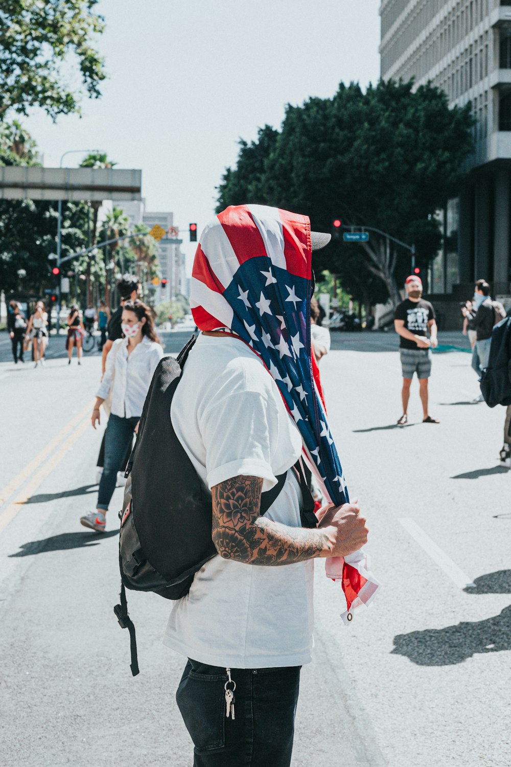 man in white shirt with brown backpack holding flag of america