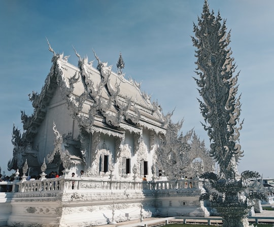 white concrete building near green trees during daytime in The White Temple Thailand