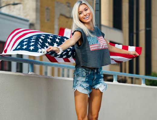 woman in black long sleeve shirt and blue denim shorts holding us a flag