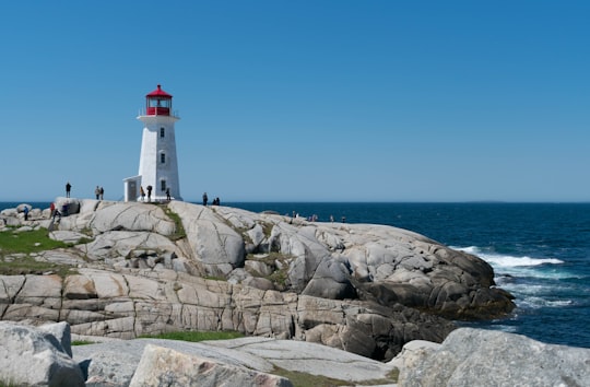 white and red lighthouse on rocky shore during daytime in Peggy's Point Lighthouse Canada