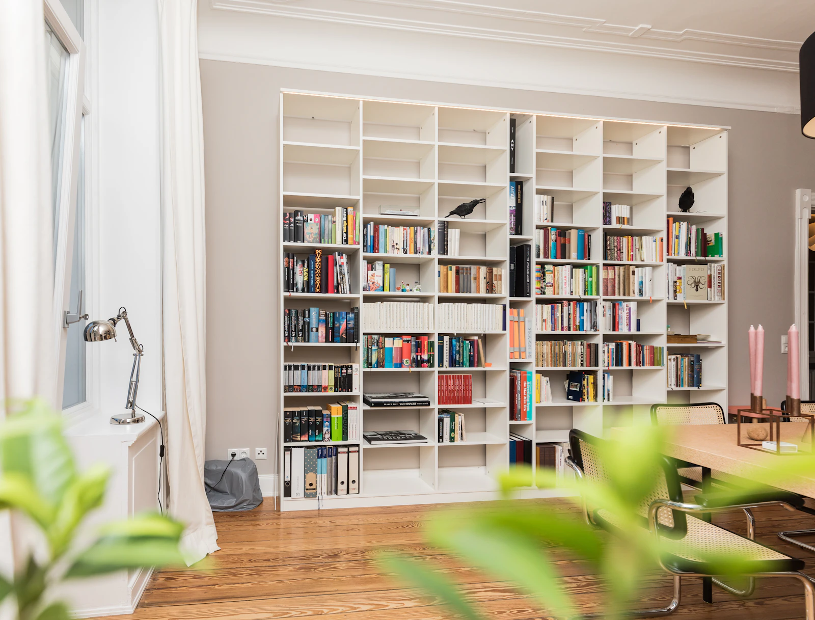 Grande bibliothèque blanche remplie de livres dans un salon lumineux au parquet
