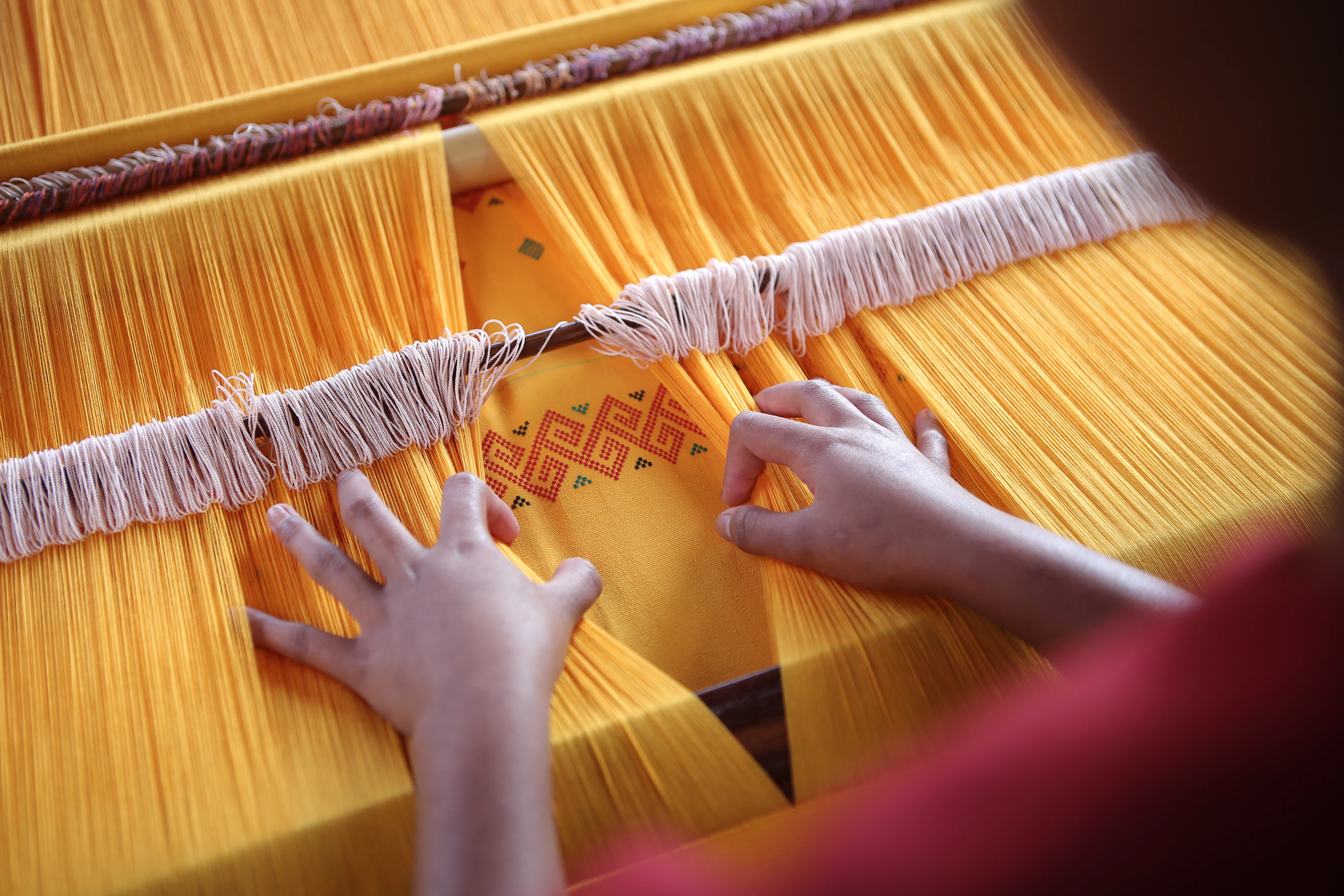 Hands weaving a patterned cloth on a traditional loom, Tana Toraja