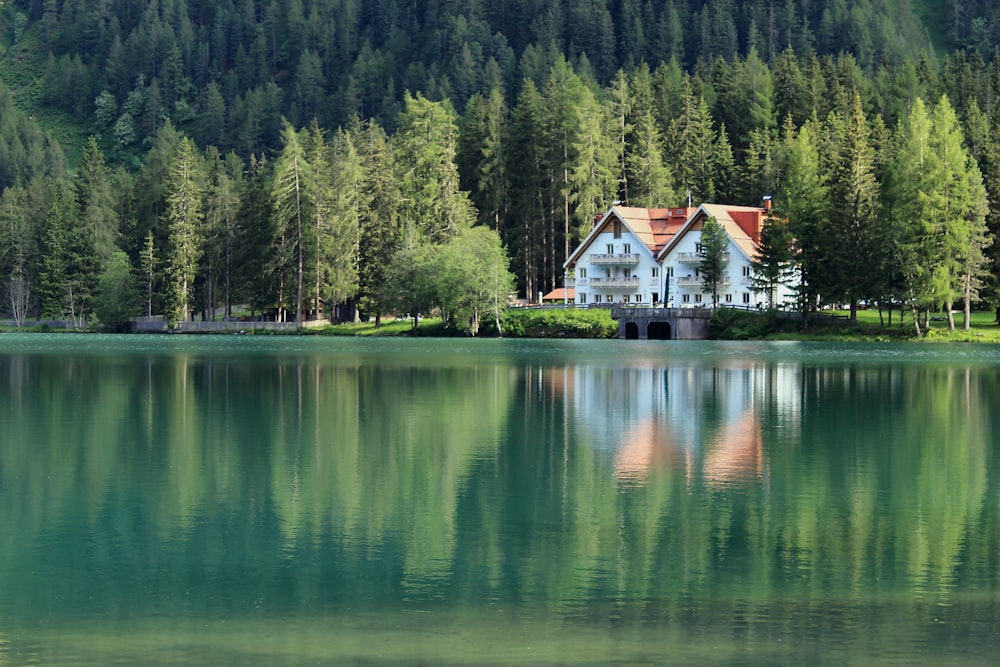weißes und braunes Haus in der Nähe von See und grünen Bäumen tagsüber