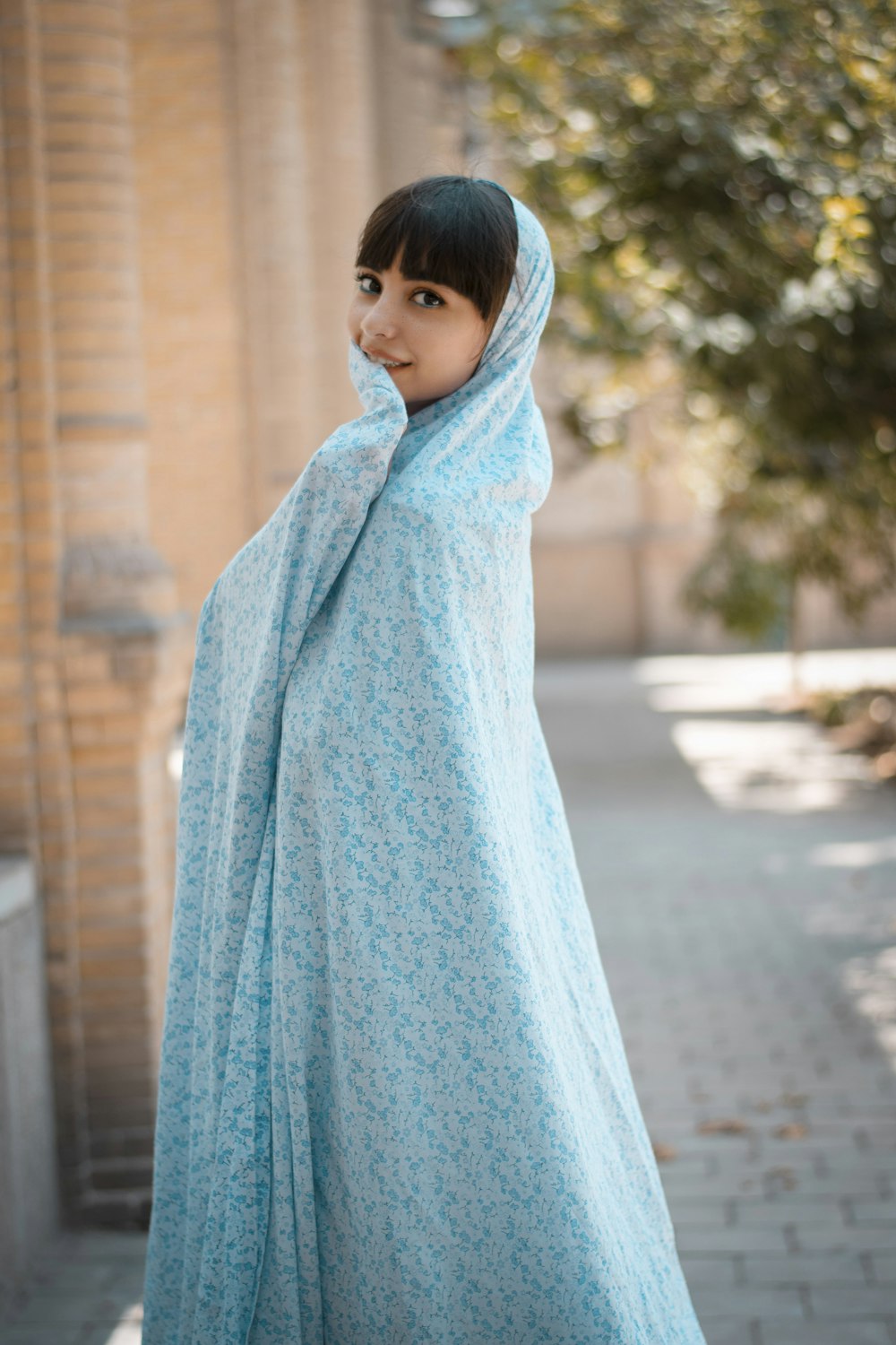 昼間、歩道に立つ青いヒジャーブの少女