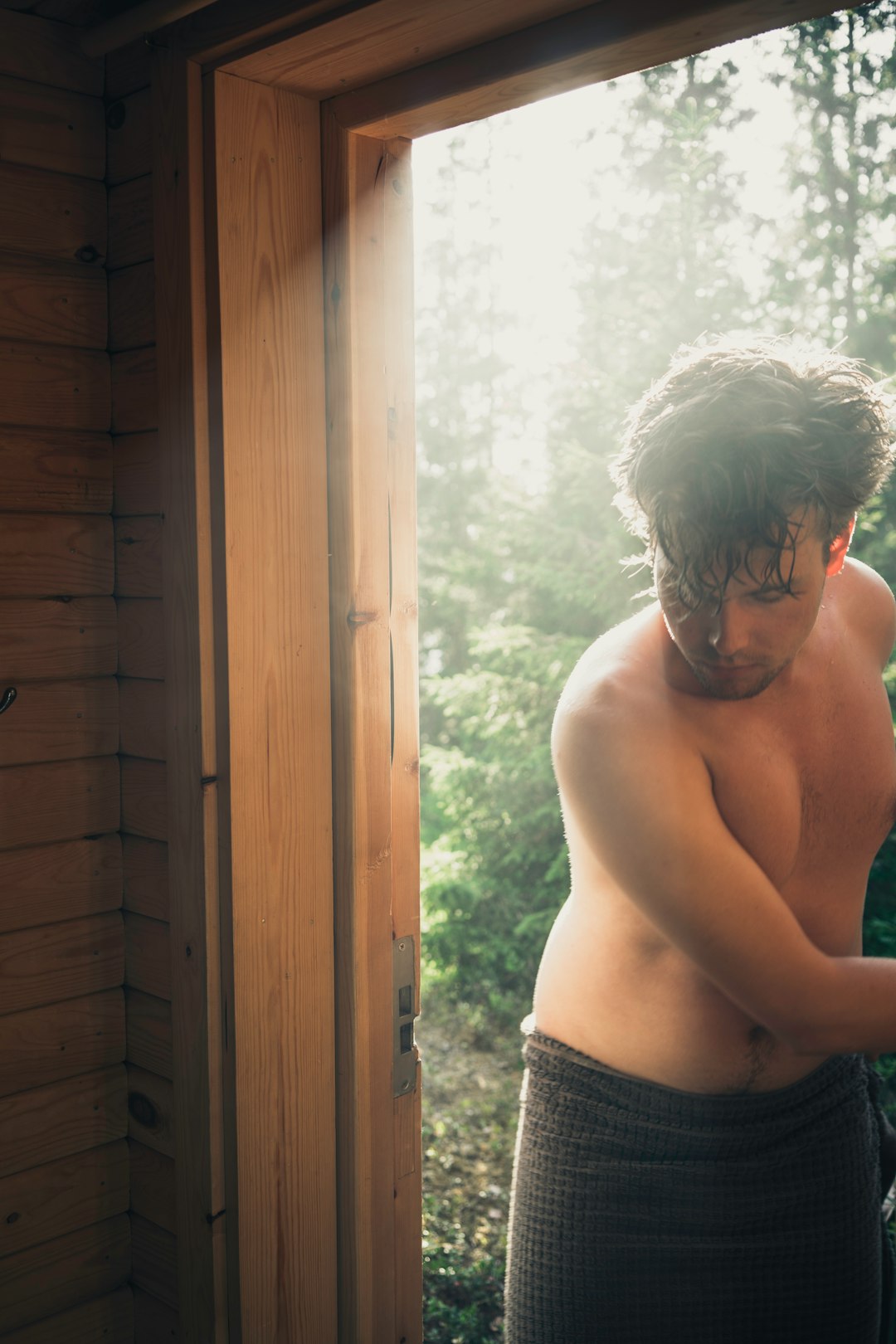 topless man in blue denim bottoms standing near brown wooden door during daytime