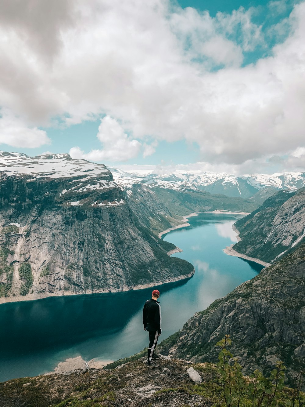 person in black jacket standing on rock formation near lake during daytime