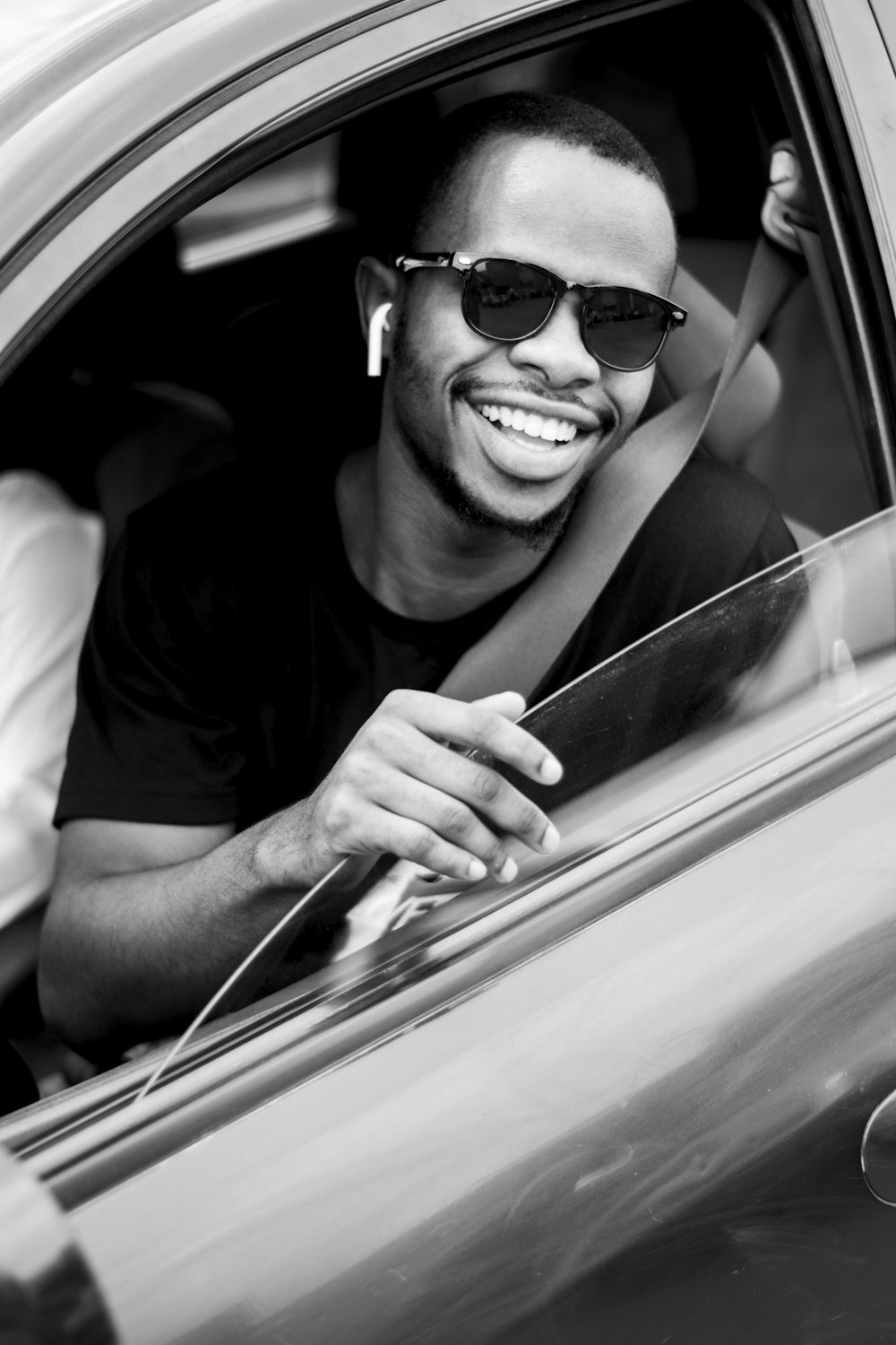 grayscale photo of man wearing sunglasses driving car