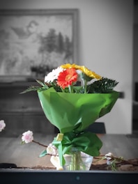 A vibrant bouquet of mixed flowers wrapped in rustic paper on a wooden table.