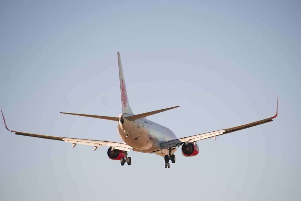 昼間の空中に浮かぶ白と赤の旅客機