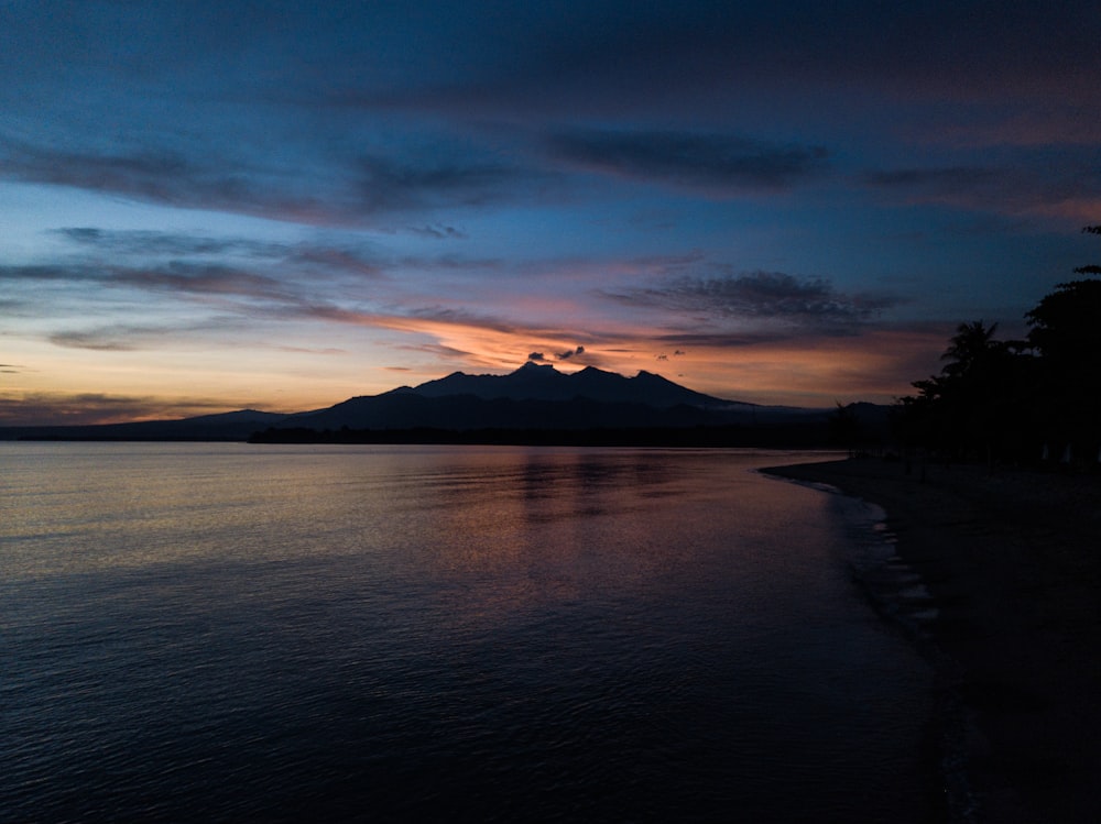 silhouette of mountain near body of water during sunset