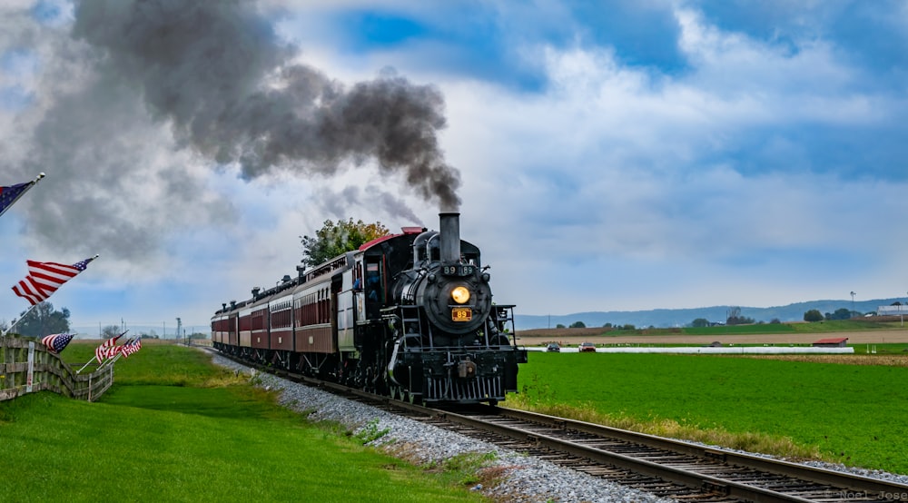 Schwarz-roter Zug tagsüber auf Bahngleisen unter weißen Wolken und blauem Himmel